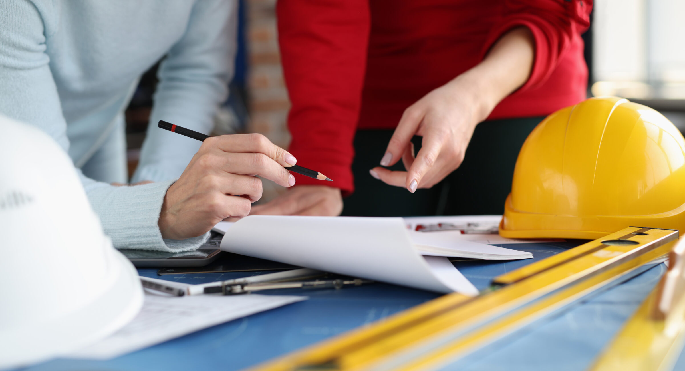 Two women looking at documents and showing them in pencil in studio. Coordination of design project concept